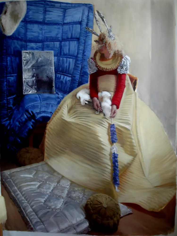 A woman wearing a garment stands indoors, surrounded by art on the wall. A blanket and plastic items are also visible in the scene.