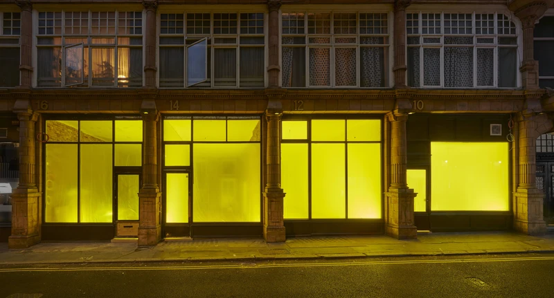 A building illuminated by a yellow light at night, featuring a window and door, set in an outdoor street environment.