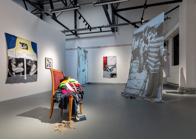 A room featuring a chair and a large picture hanging on the wall, suggesting an art exhibition or gallery setting.