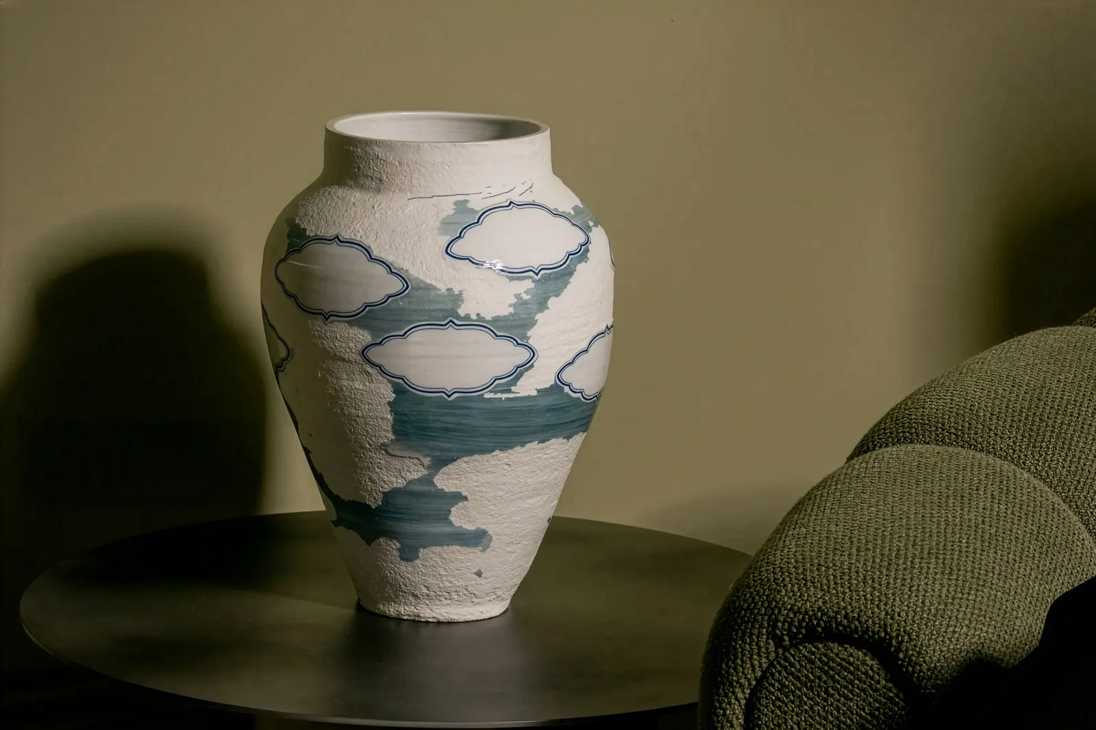 A ceramic vase placed on a wooden table, surrounded by a simple indoor setting, representing still life photography.