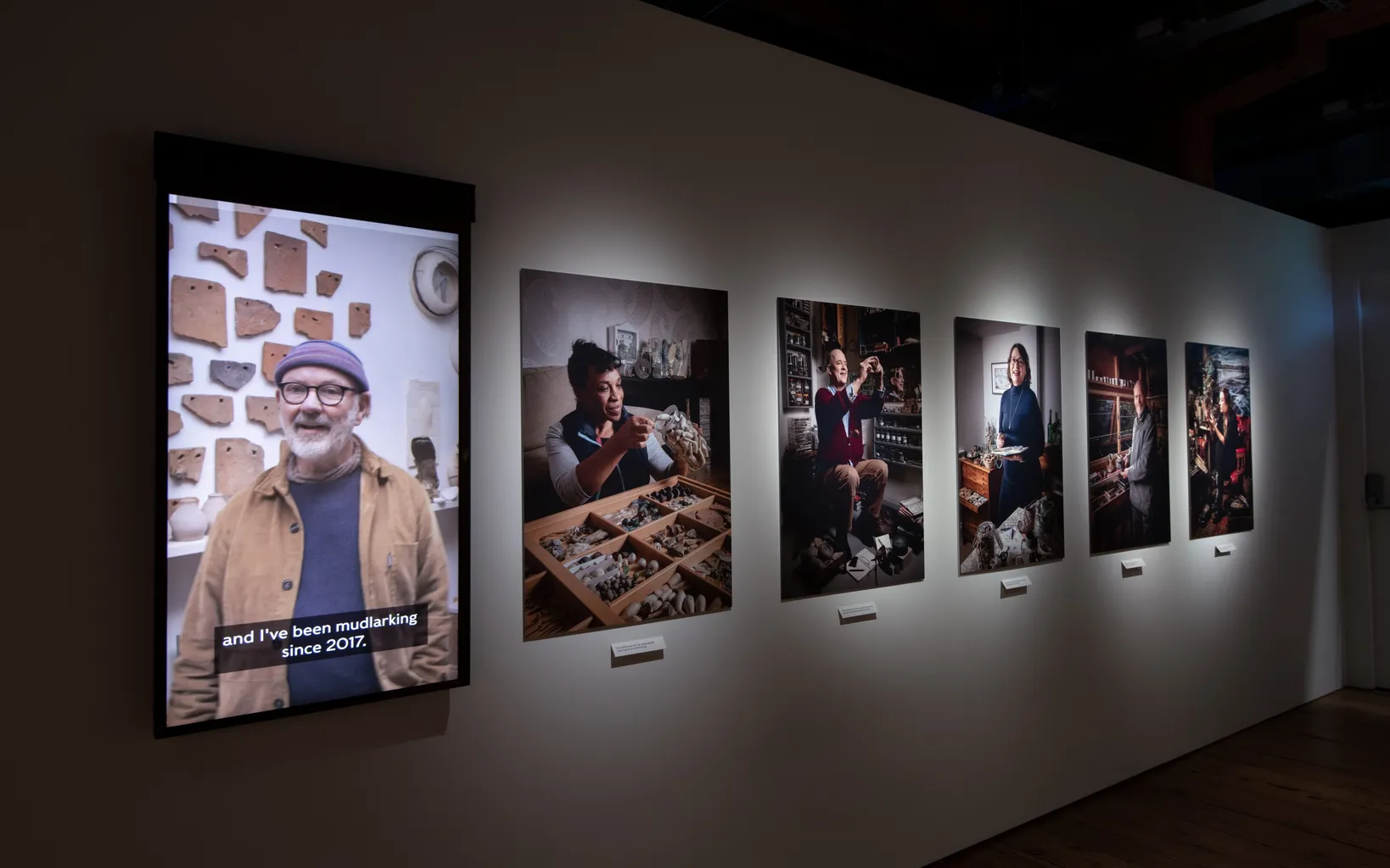 Alt text: A wall displaying various framed pictures of people in an indoor gallery setting.