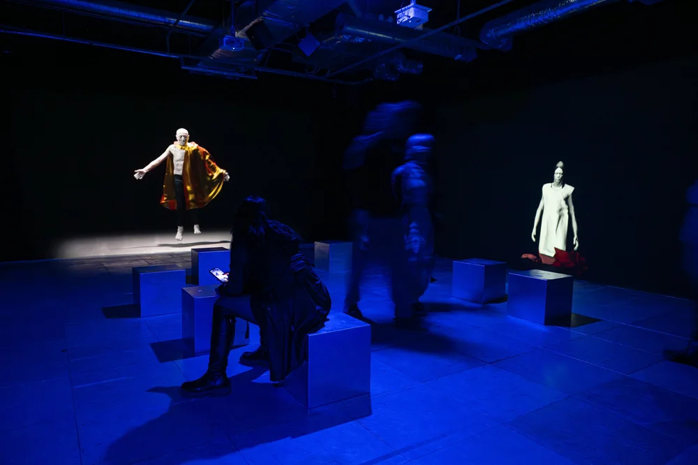 A group of people gathered in a room surrounded by theatrical scenery, with a statue present, engaged in dance and artistic activities indoors.