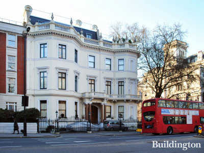 Elegant white Victorian building with decorative cornices, featuring a red double-decker bus parked nearby on a city street. | 2017