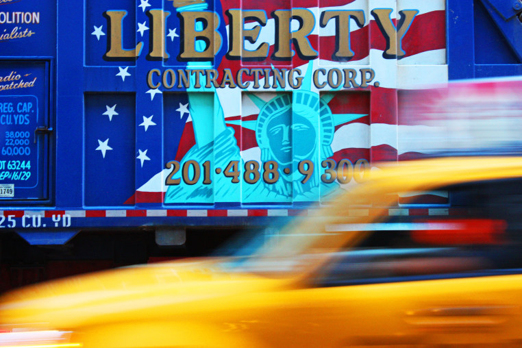 A yellow taxi in motion in front of a building displaying various signs and text.