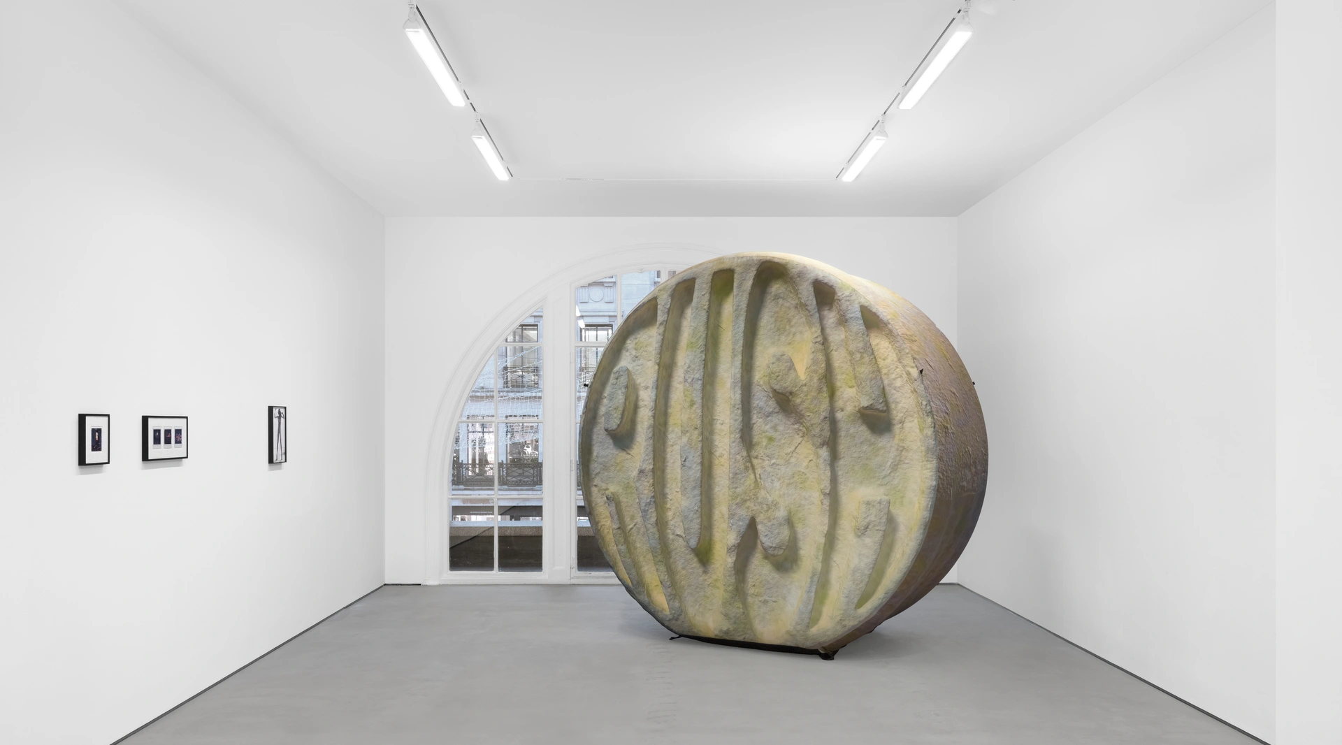 A large stone sculpture is positioned in the center of a room with a barrel on the floor. The walls and ceiling are visible, highlighting the indoor setting.