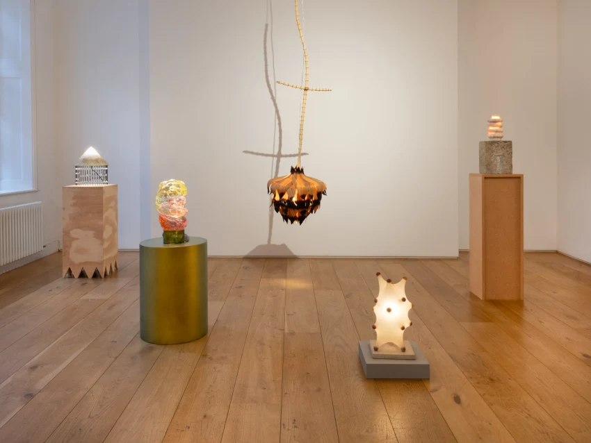 Alt text: A room featuring several sculptures displayed on a floor with wood and laminate flooring, complemented by decorative items such as a vase and a candle against an interior wall.