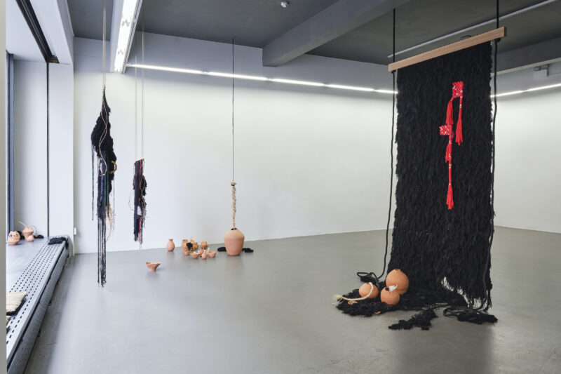 A room featuring a black cloth draped over various objects, with a wall in the background. The flooring is visible, showcasing the floor surface and various pieces of footwear arranged artfully within the space.
