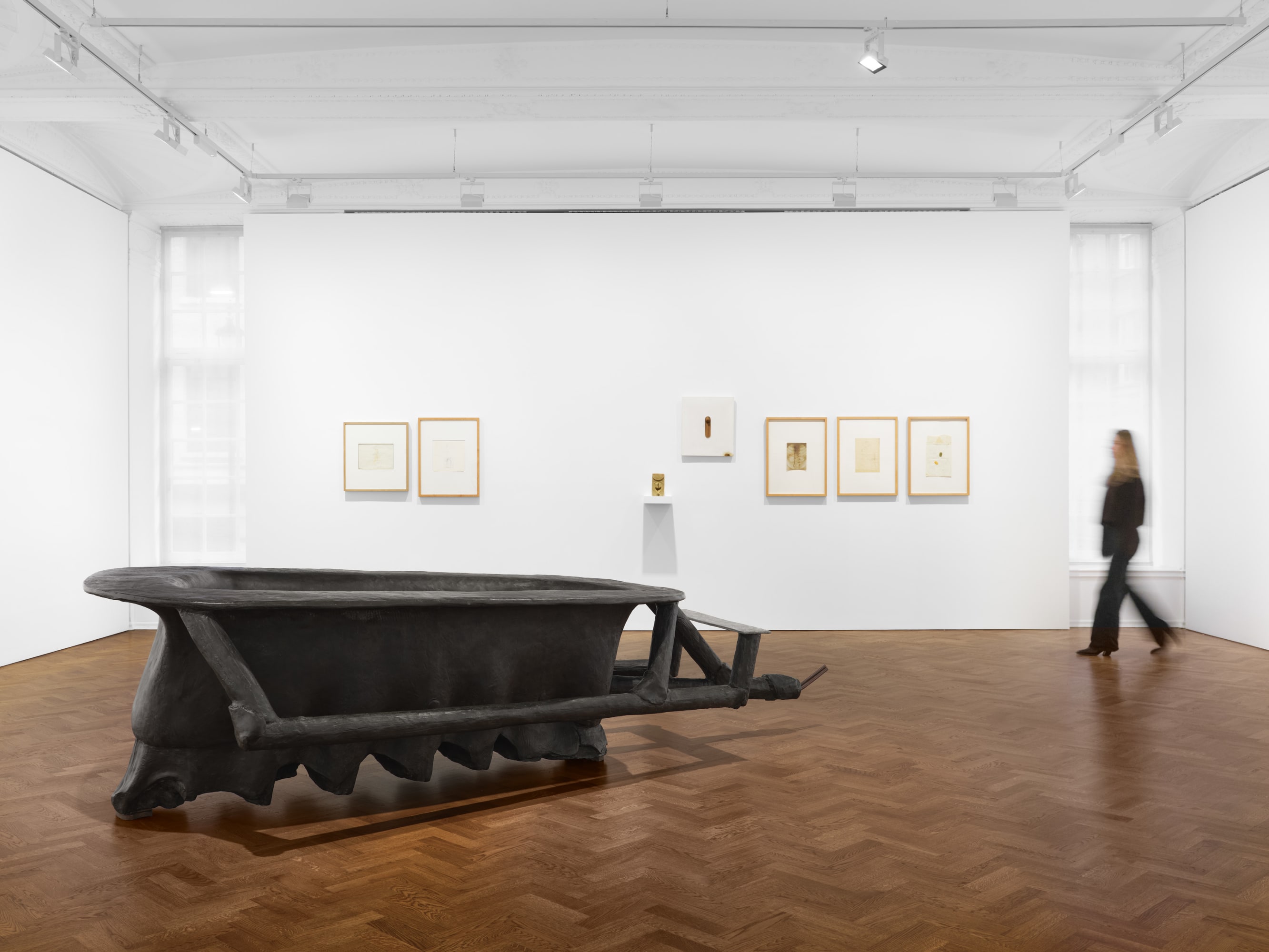 A man walking past a large black object in a museum, surrounded by walls and various art pieces. The interior design includes flooring, a picture frame, and possibly furniture like a couch, all within a well-lit hall with an ornate ceiling. | 2026 Thaddaeus Ropac