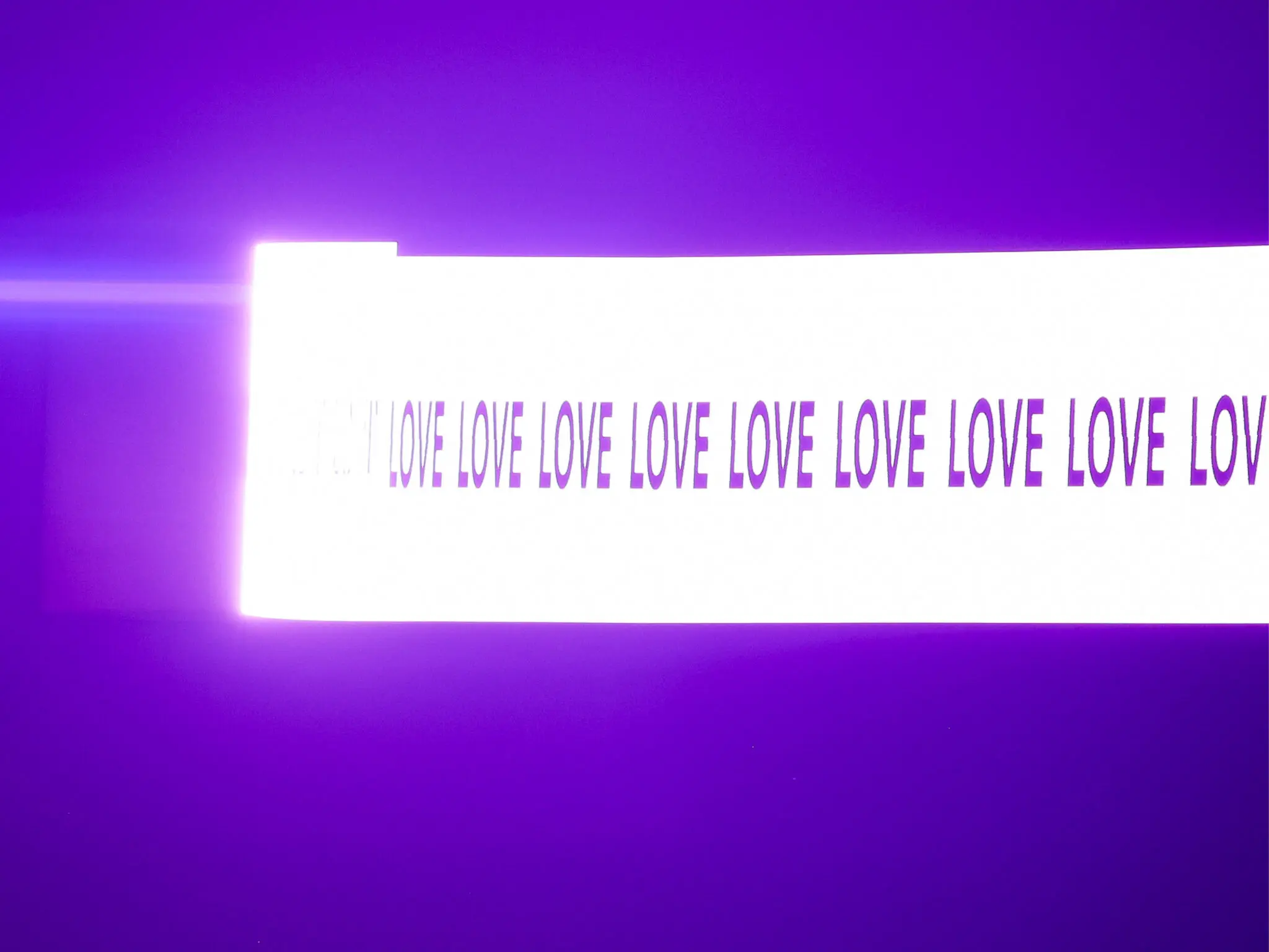 A bright, illuminated sign displays the repeated word "LOVE" in bold, black letters against a vibrant purple background.