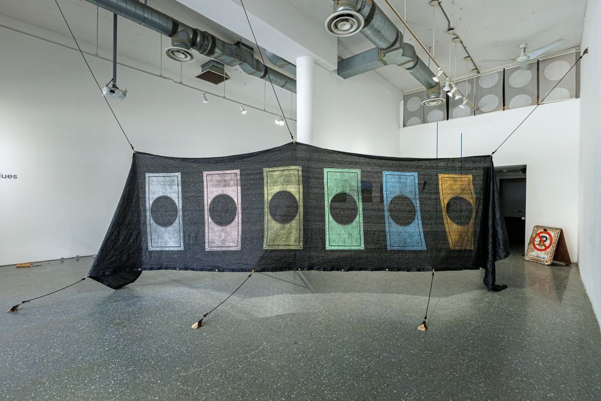 A large black fabric installation with colored circular patterns, displayed in an art gallery space.
