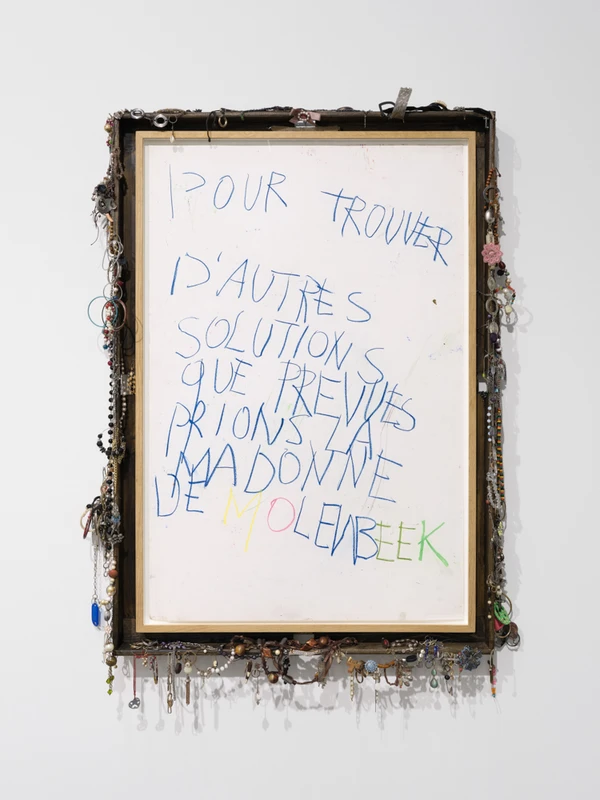 Text on a framed artwork: "POUR TROUVER D'AUTRES SOLUTIONS QUE PREVISES PRIONS Z'EN MADONNE DE MOLEENBEEK" with various decorative elements around the frame.