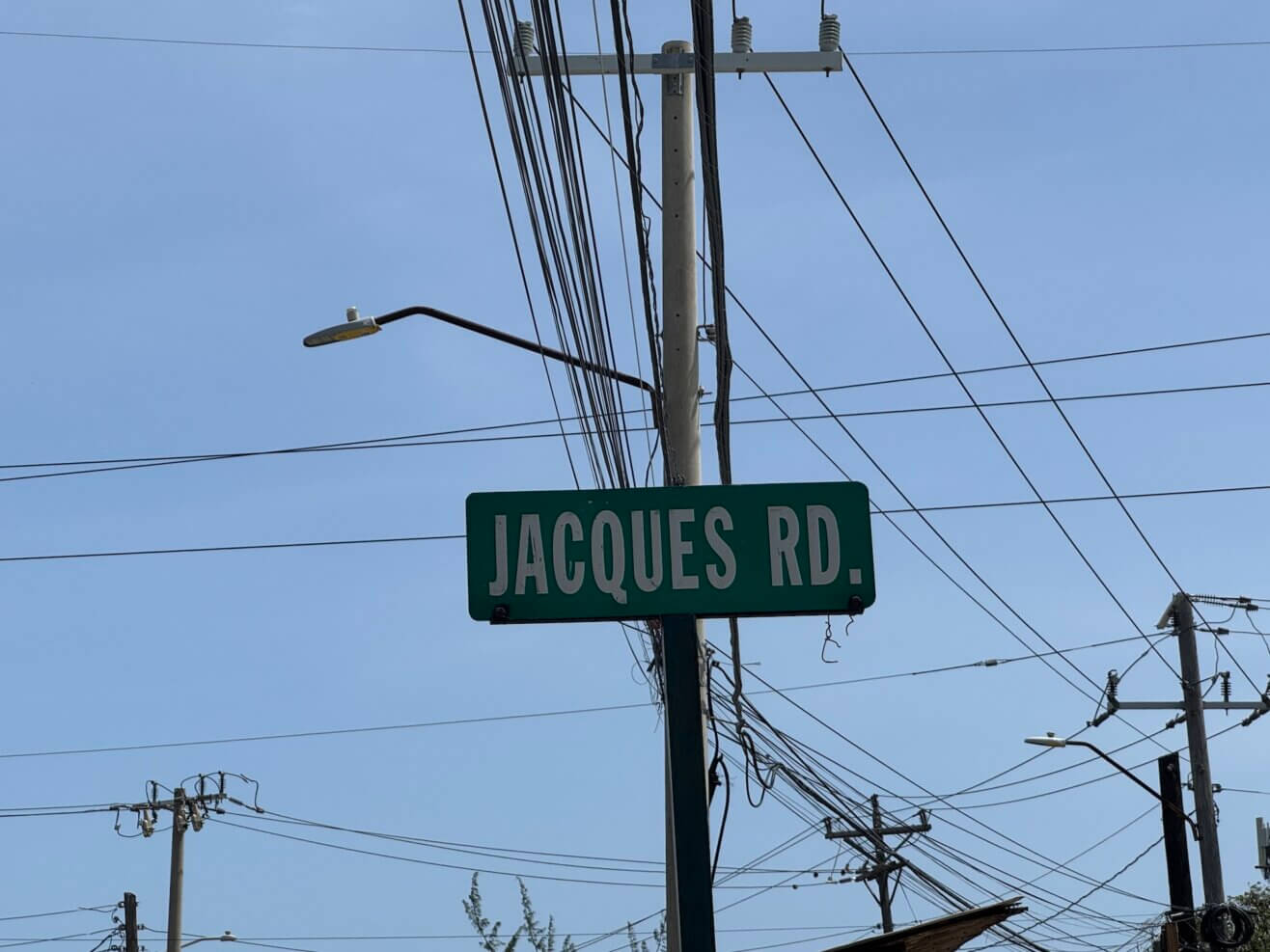 Street sign for Jacques Rd. against a backdrop of power lines and a blue sky.