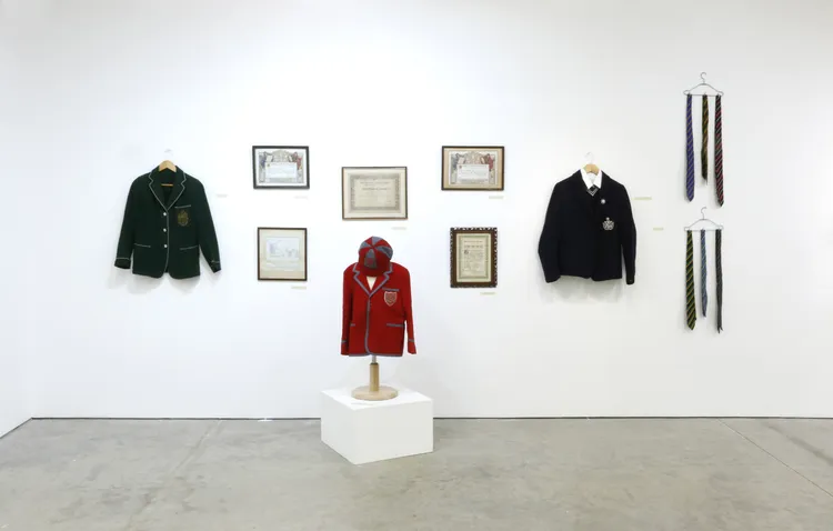 A display of various jackets and ties on a white wall, with framed documents surrounding them.