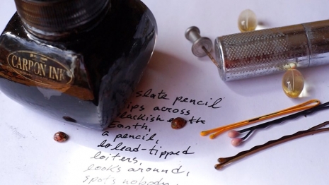 A bottle of ink, a mechanical pencil, and some hairpins are placed on a piece of paper with handwritten text.