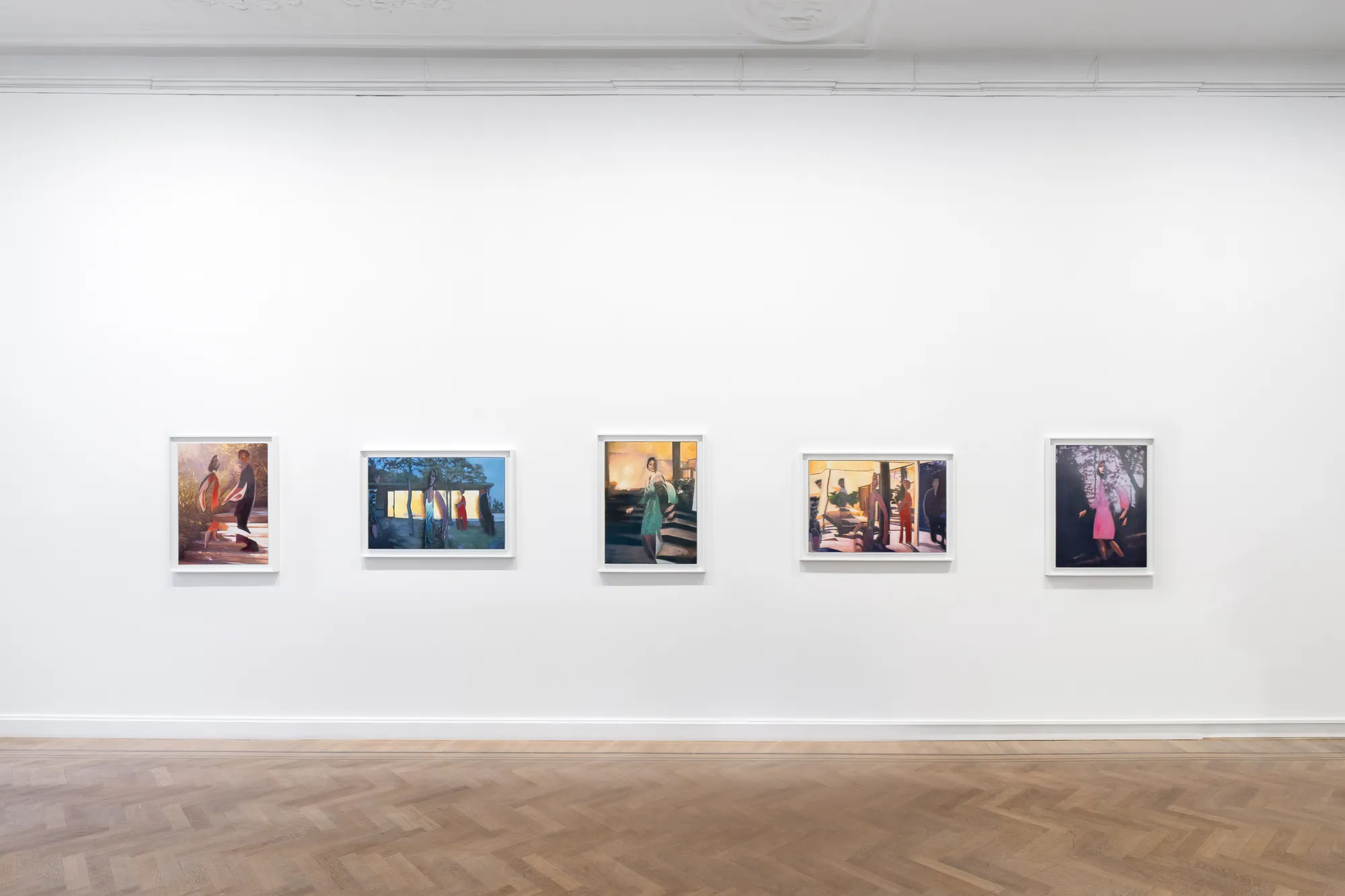 Five framed artworks are displayed on a white wall in an art gallery. The floor is wooden, and the space is well-lit.