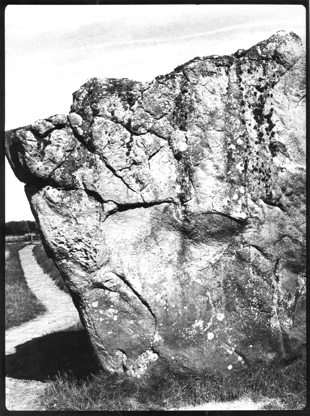 A large rock formation with a rugged texture, situated near a walking path surrounded by grass. | 2026 HackelBury Fine Art