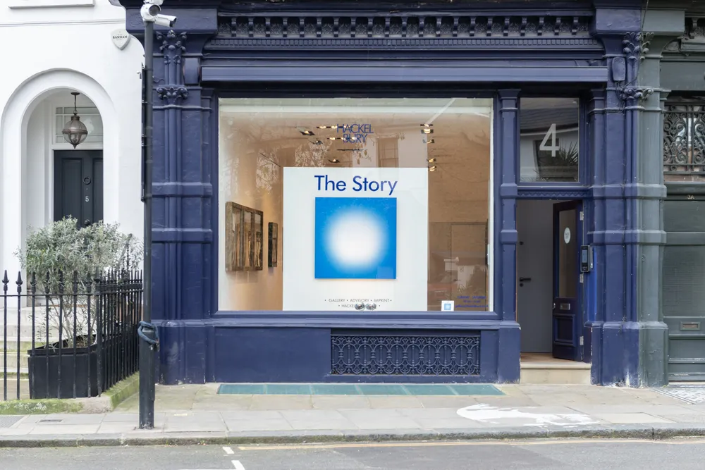 A storefront with a large window displaying an art piece titled "The Story" and minimalistic decor inside.