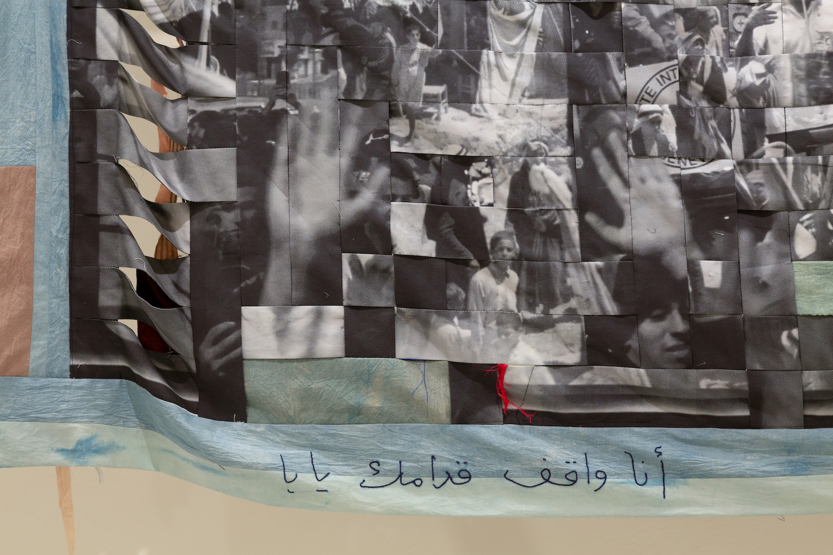 A collage of black and white images depicting hands raised in various positions, integrated with textile elements. Below the images, there is Arabic text that translates to "I stand with you."