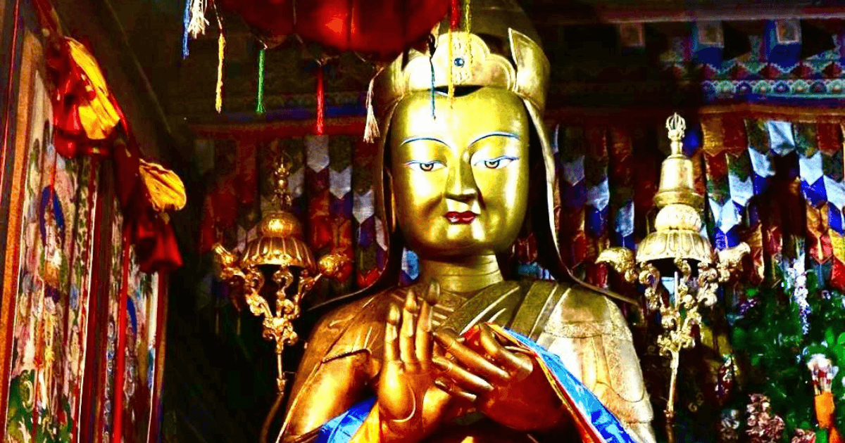 A golden statue of a Buddhist figure with a serene expression, adorned with traditional ornaments and set against a colorful, decorative backdrop.