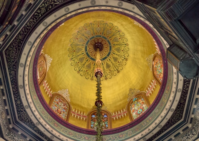 A view of the intricate, colorful ceiling of a dome with floral patterns, detailed frescoes, and stained glass windows.