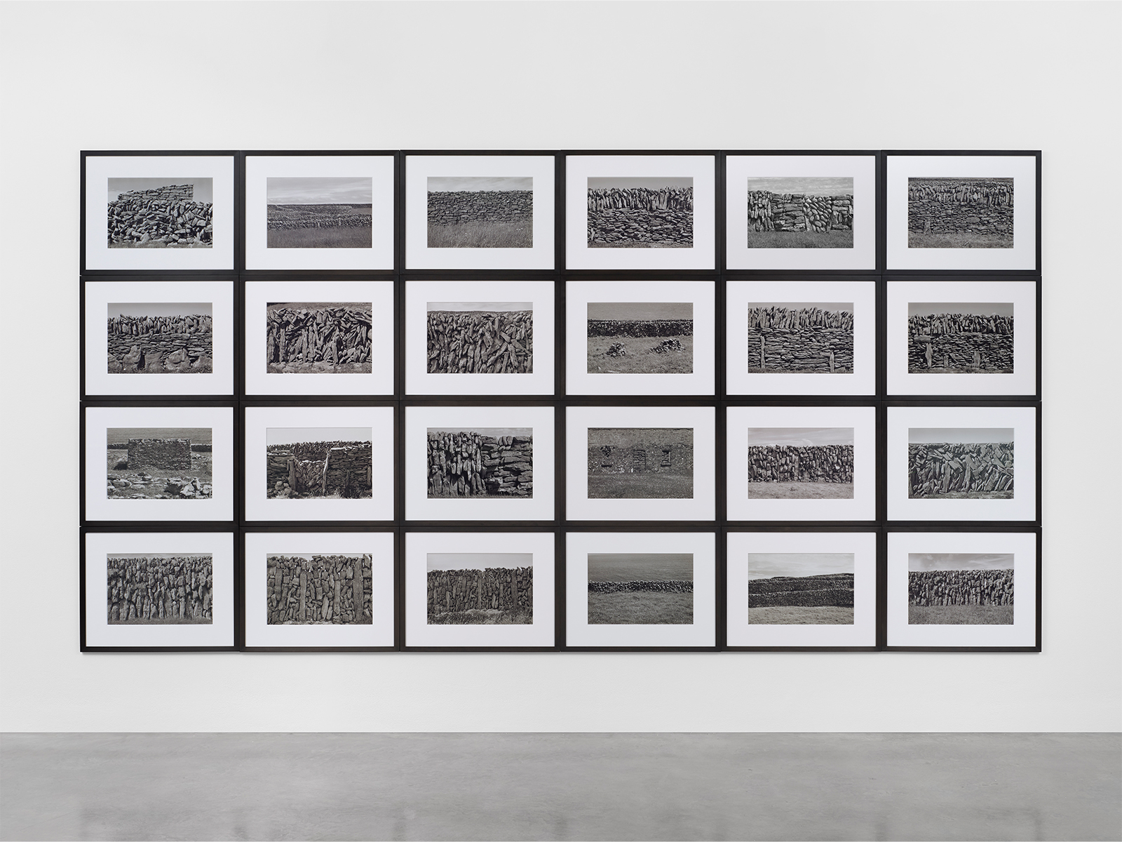 A gallery wall displaying a grid of black and white photographs in black frames, showcasing various textured landscapes or abstract patterns.