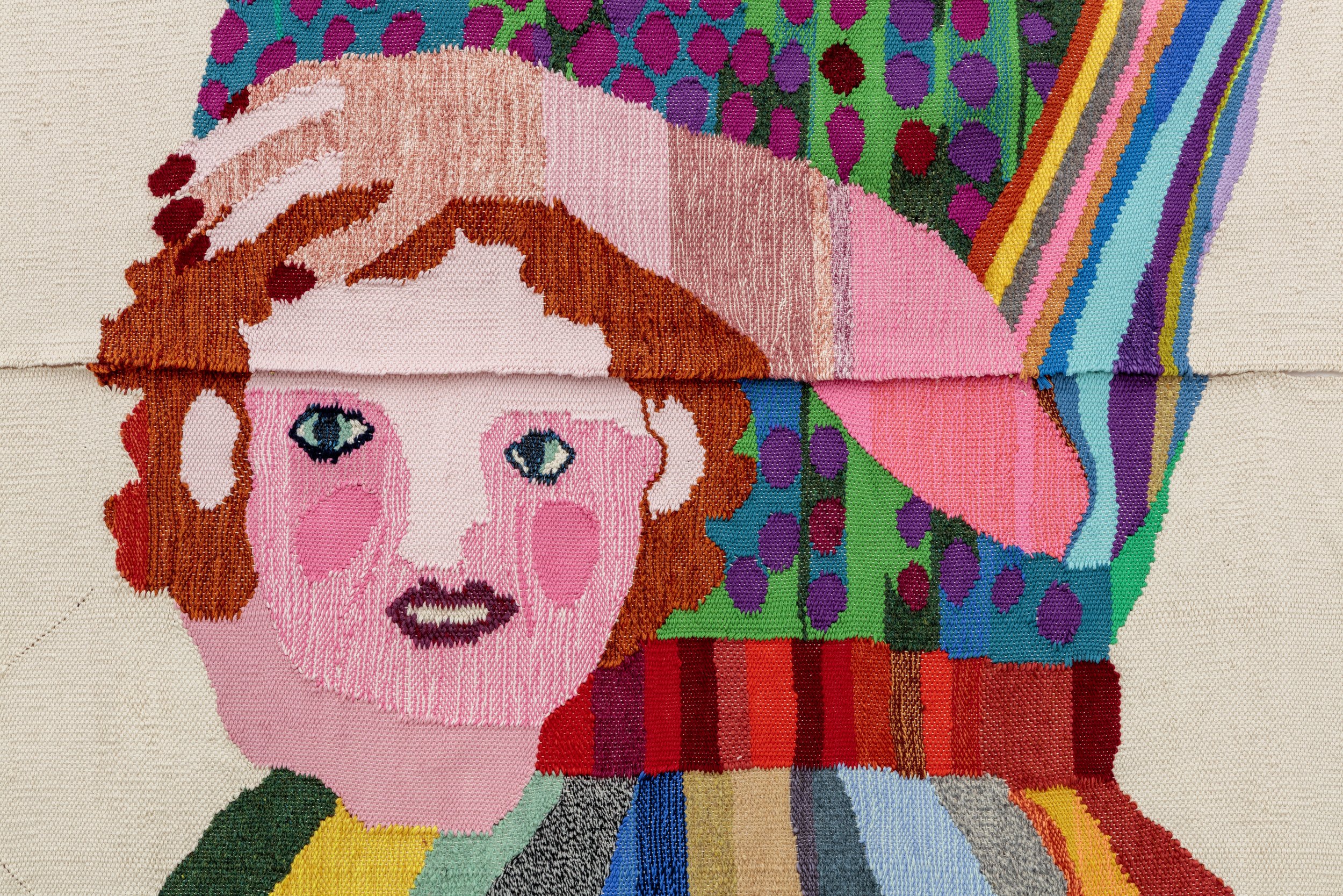A colorful textile artwork featuring a stylized portrait of a person with rosy cheeks and large blue eyes, being gently touched by a hand. The background includes vibrant patterns in various colors. | 2026 Maximillian William