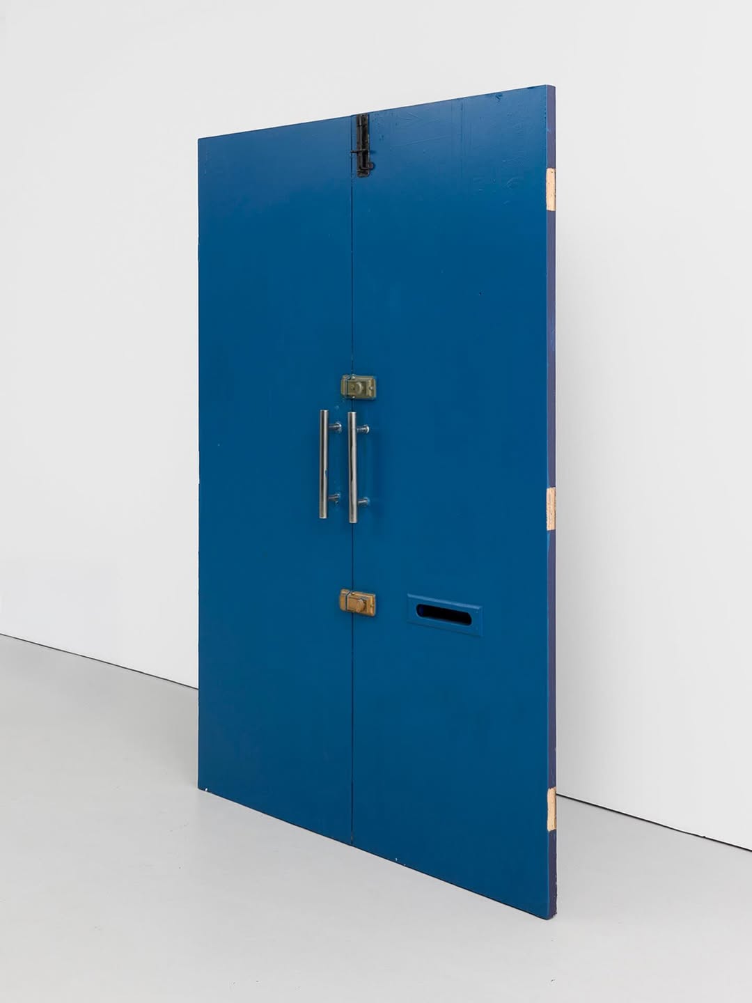 A large blue door with two handles, set against a white wall.