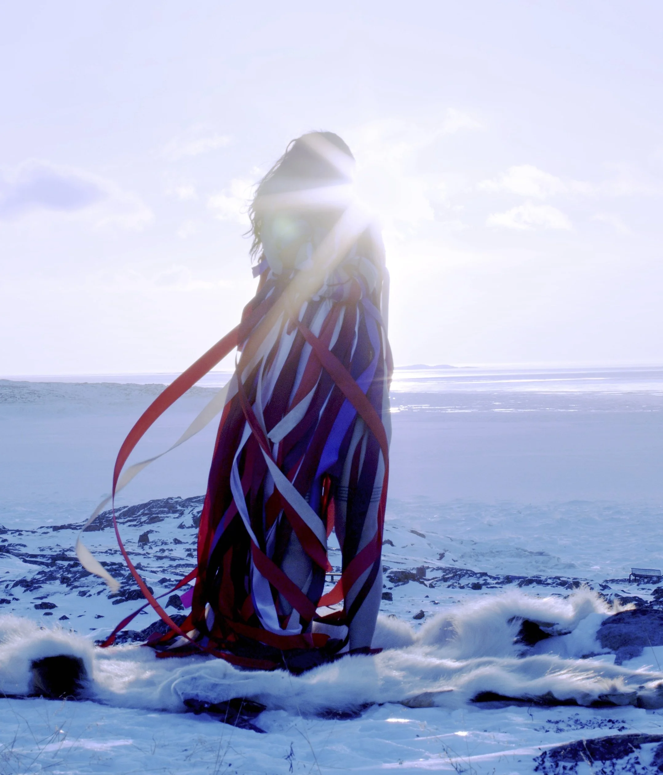 A figure stands in a snowy landscape, wearing a flowing garment with long, colorful ribbons that trail behind them. The sun shines brightly in the background, creating a halo effect around the figure. | 2026 Mimosa House