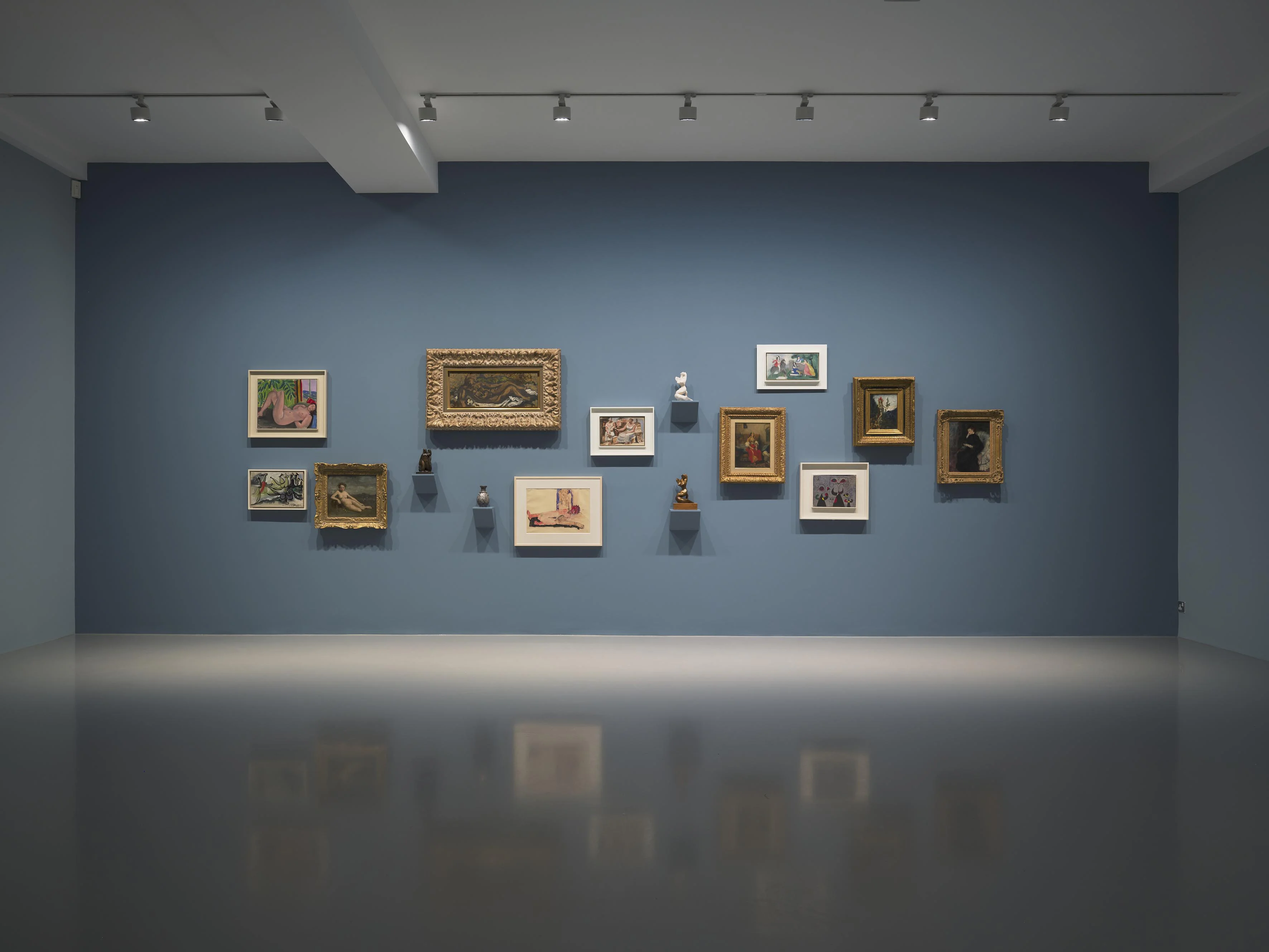 A gallery wall featuring an arrangement of various framed artworks against a blue background, with multiple styles and sizes of frames.