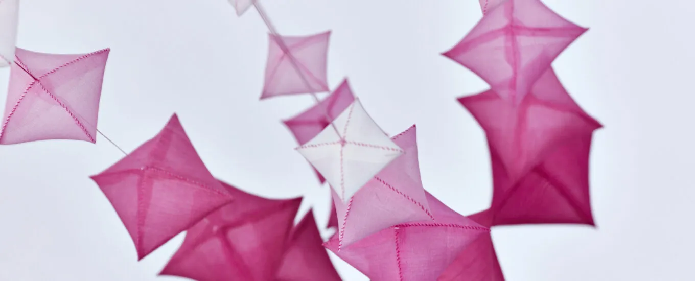 Colorful geometric shapes in shades of pink and white, suspended against a light background.