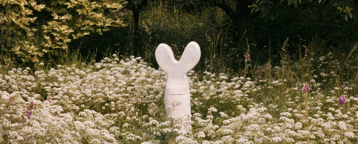 A white sculpture resembling a rabbit stands amidst a field of wildflowers.