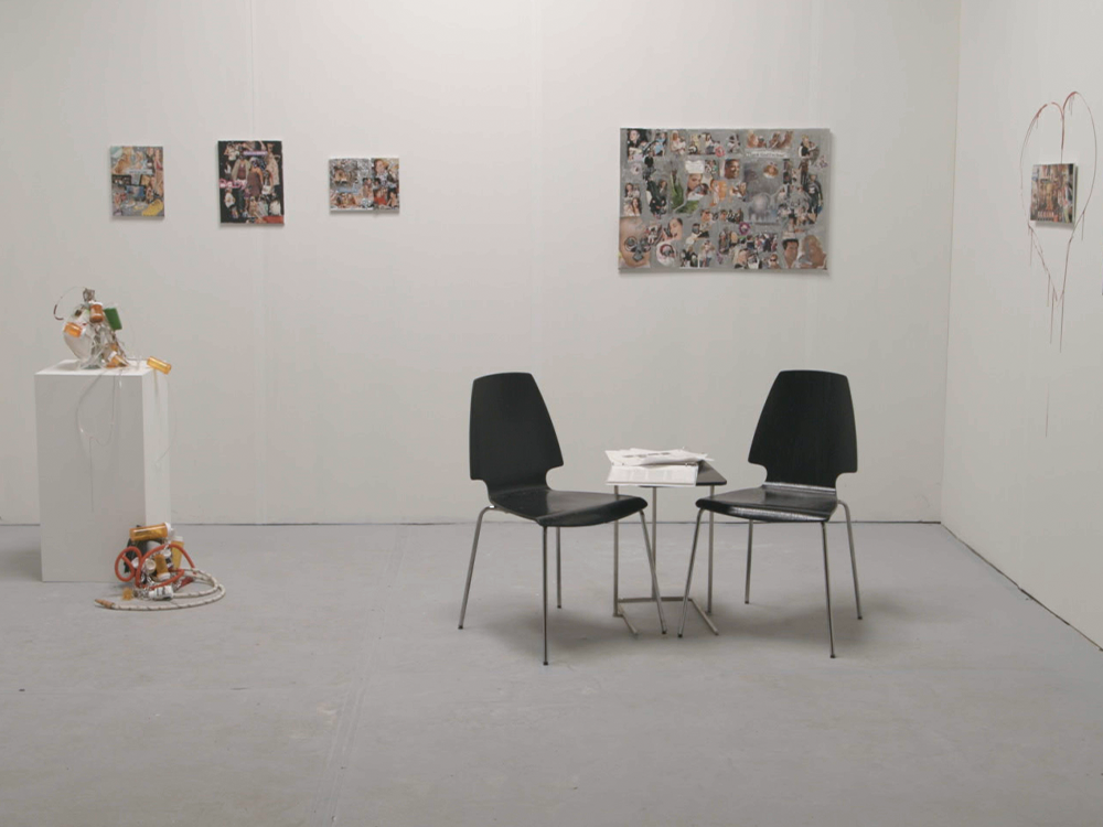 Two black chairs at a small table in an art gallery, with several artworks hung on the white walls.