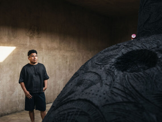 A person standing next to a large black sculpture in an industrial-looking space. | 2026 Whitechapel Gallery