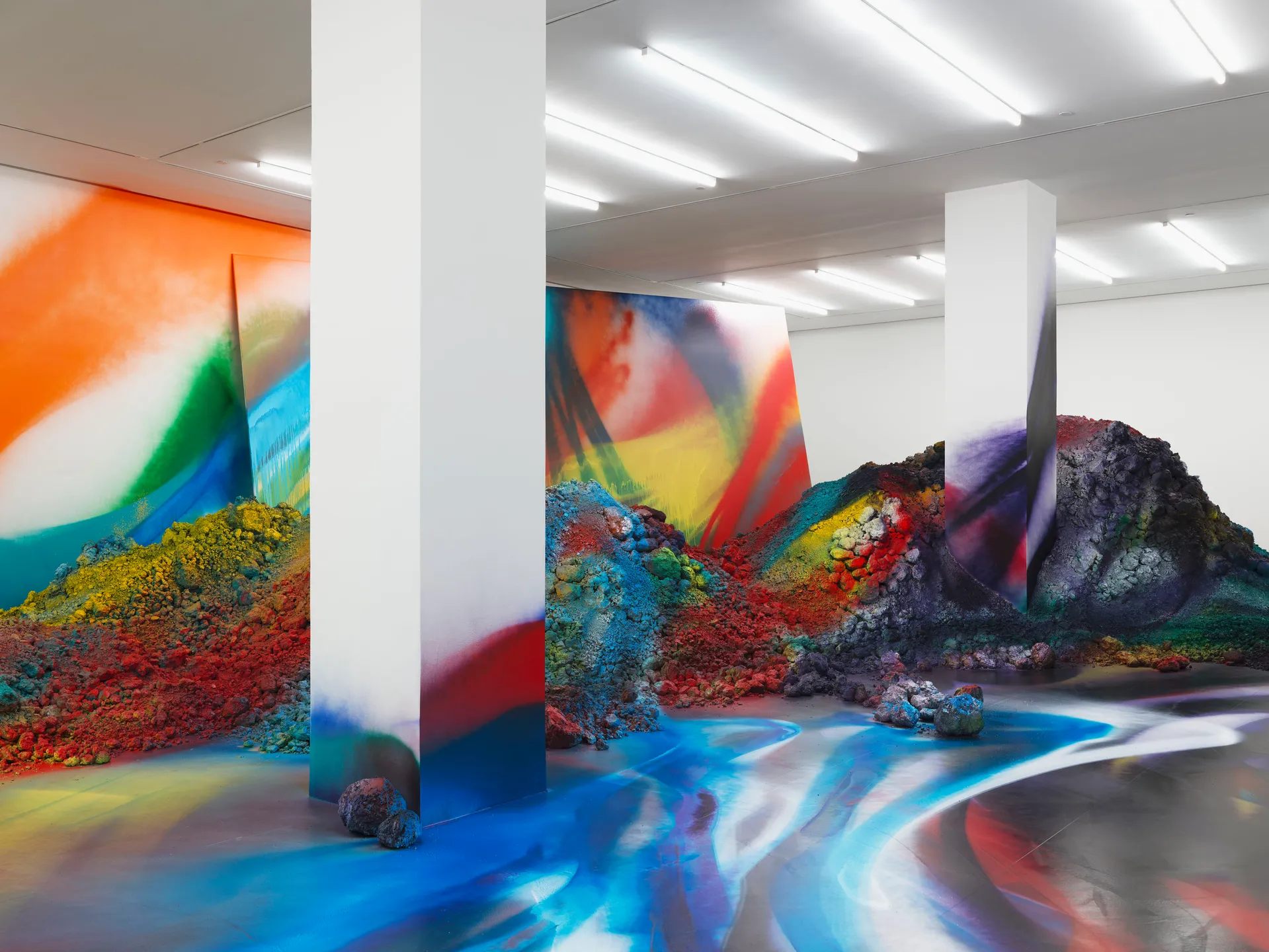 An art installation featuring colorful, abstract patterns on the walls and floor, with textured mounds of vibrant materials creating a dynamic environment. | 2026 White Cube