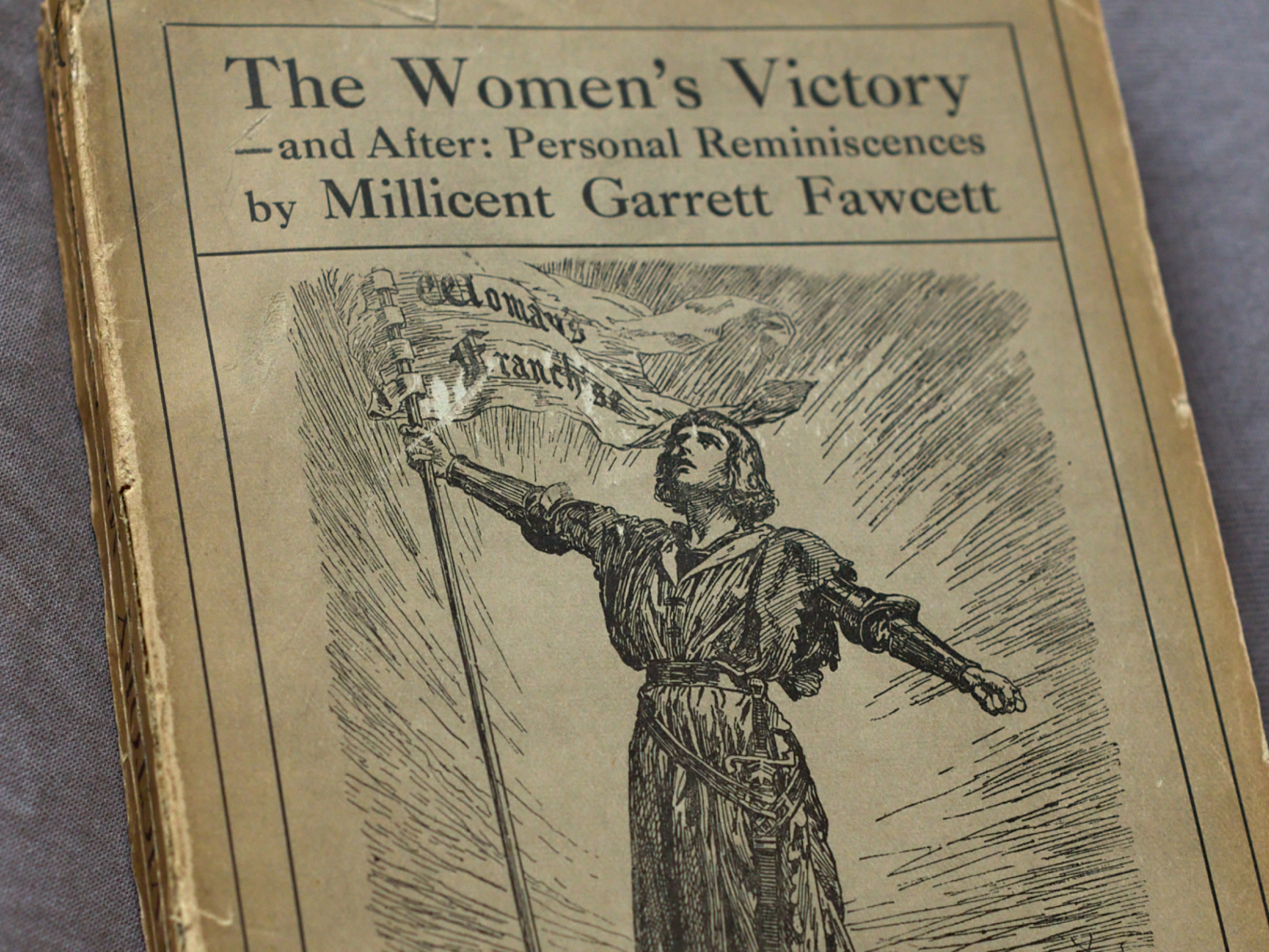 A vintage book cover titled "The Women's Victory—and After: Personal Reminiscences" by Millicent Garrett Fawcett, featuring an illustration of a woman holding a flag.