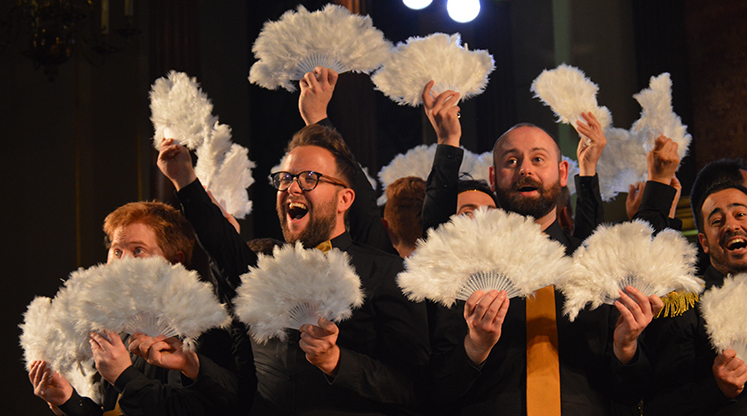 A group of performers holding white fans, smiling and enjoying a lively moment on stage.
