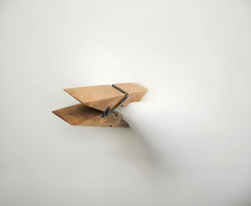 A wooden object shaped like an arrowhead protruding from a white wall.