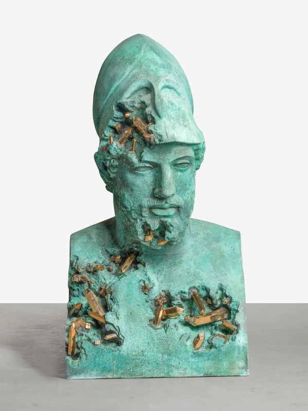 A greenish-blue sculpture of a bust wearing a helmet, showing signs of damage with wooden elements protruding from various areas.
