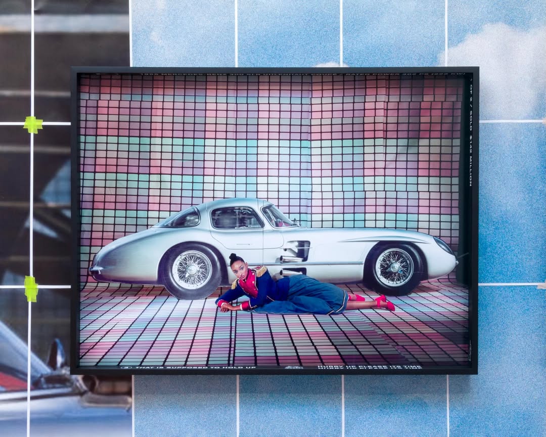 A woman in a colorful outfit poses next to a vintage silver car against a backdrop of pastel-colored grid patterns.