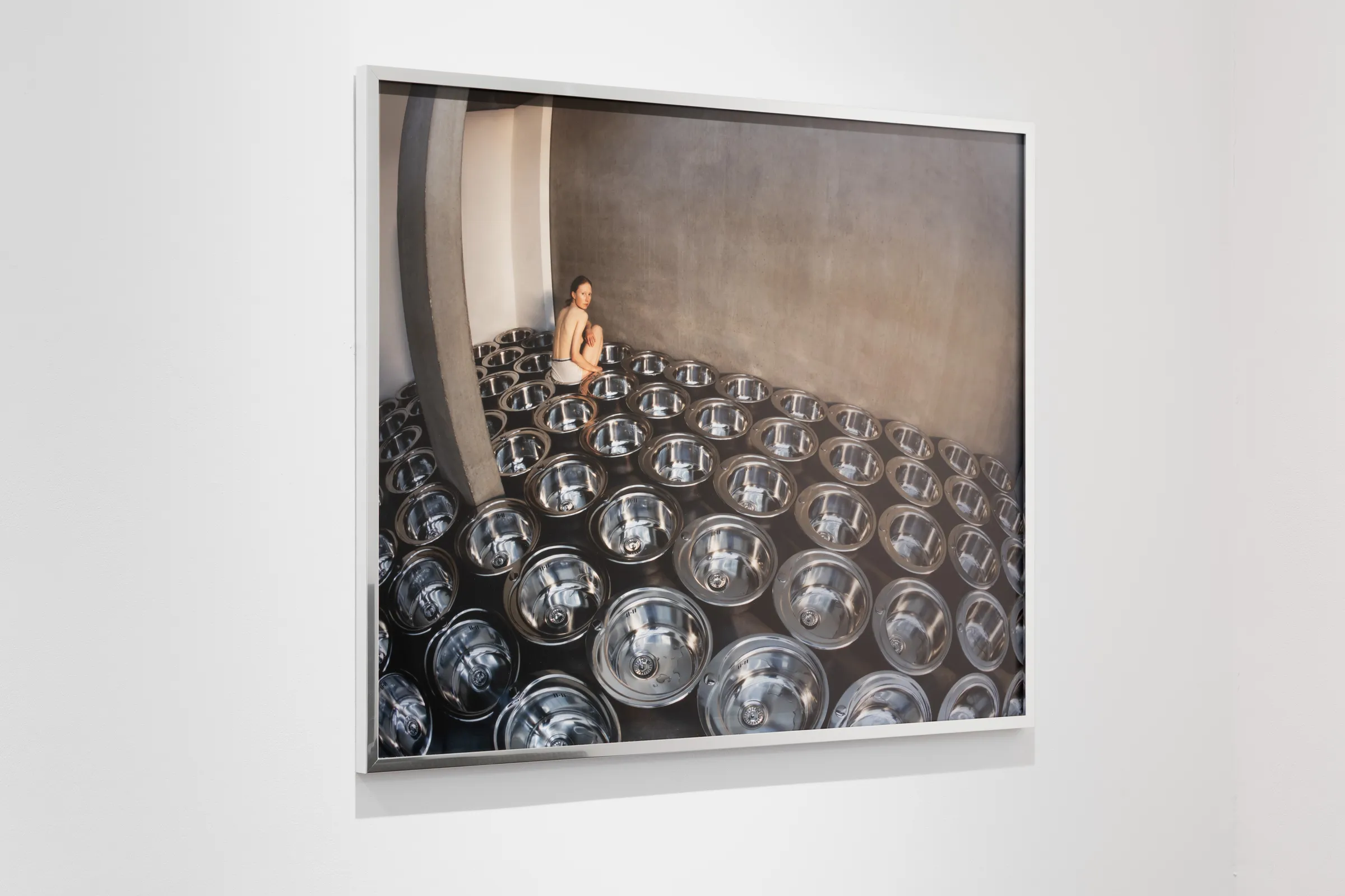 A person sitting among a large number of round reflective objects in an enclosed space.