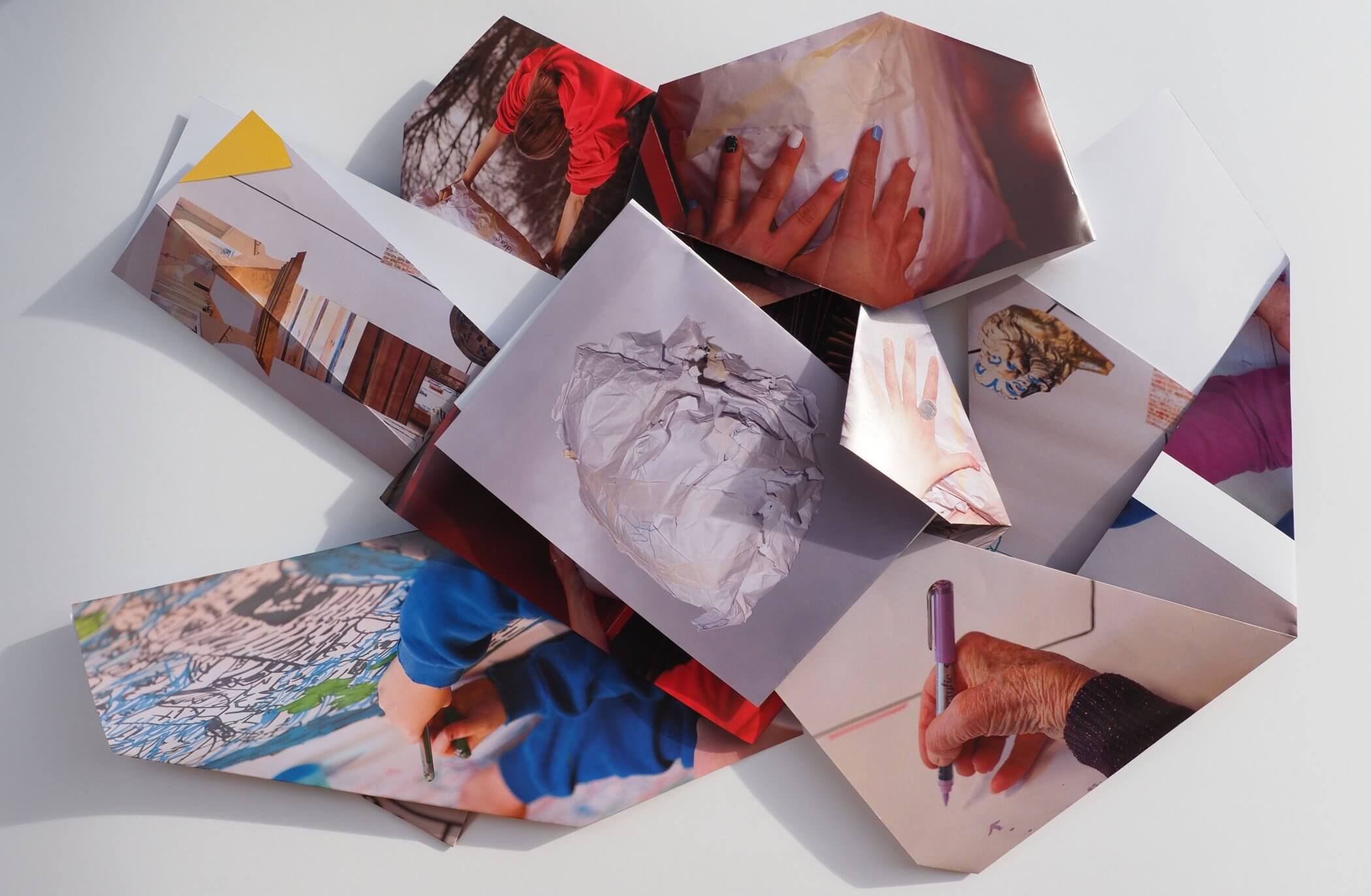 A collection of various photographs scattered and overlapping on a white surface, showcasing hands, art materials, and abstract images.