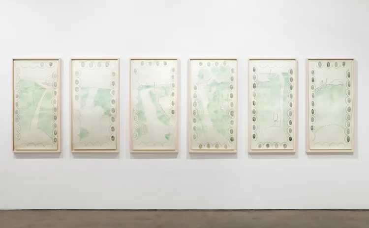 A series of six framed artworks with light green and beige watercolor designs on a white wall.