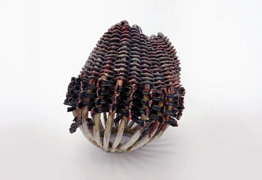 A sculptural piece resembling a crown or headpiece, made of coiled materials in an array of colors, predominantly earthy tones, with a textured surface. The structure is bulbous and shows intricate patterns created by the coils. | 2026 Larkin Durey