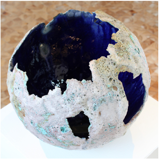 A broken spherical sculpture with a dark blue interior and a textured, weathered exterior featuring areas of corrosion and pitting.