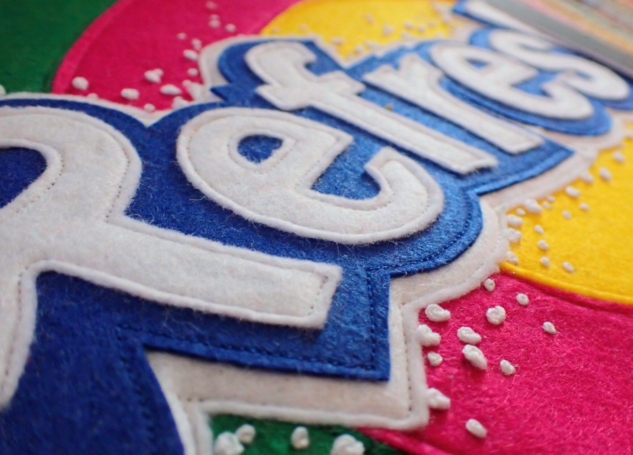 Close-up of colorful felt letters spelling "Refresh," with blue and white text on a bright background.