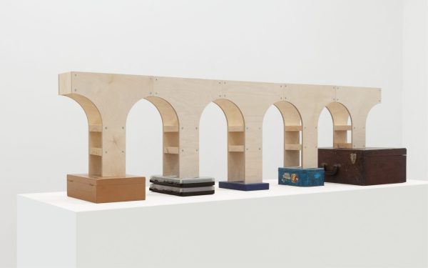 A wooden shelf with multiple arch-shaped openings on top, displaying various boxes below it.