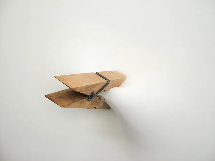A wooden paper airplane emerging from a wall, with smoke or mist trailing behind it.