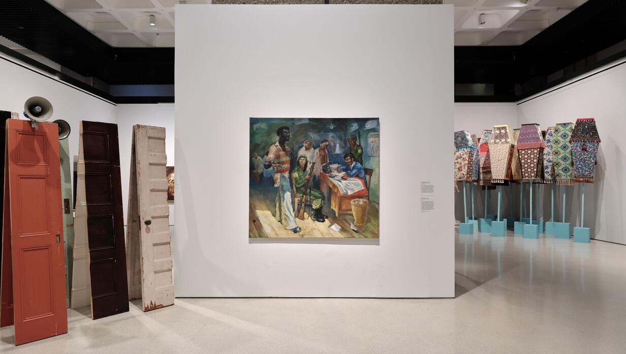 A gallery space featuring a painting on a white wall surrounded by various art pieces, including colorful sculptures resembling doors.