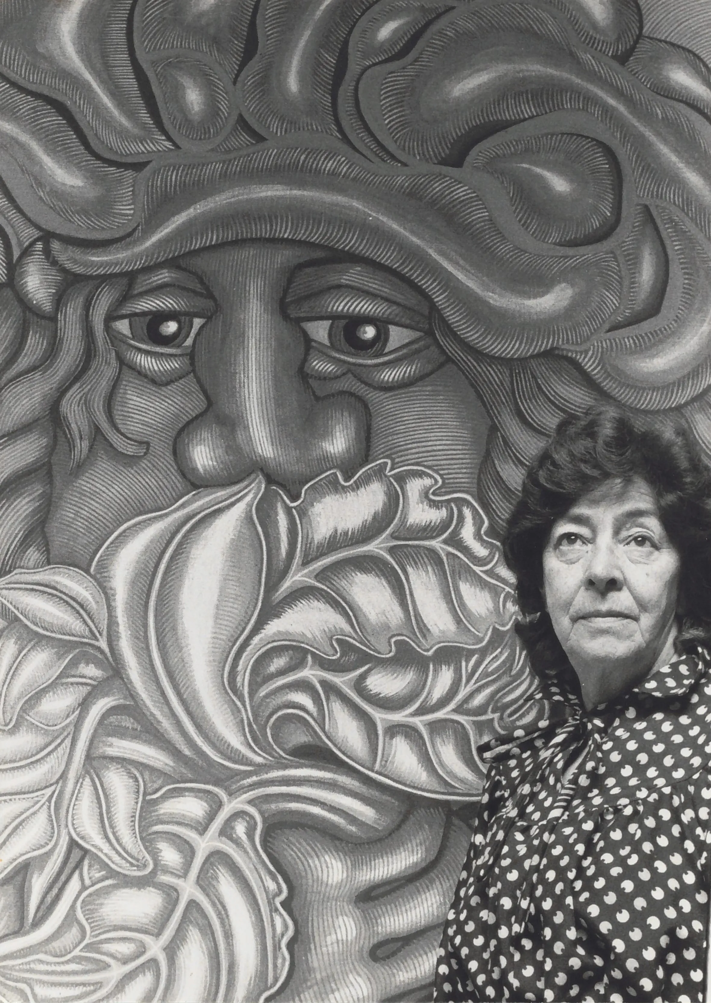 A woman standing in front of a large, intricately detailed mural featuring a face and floral elements.