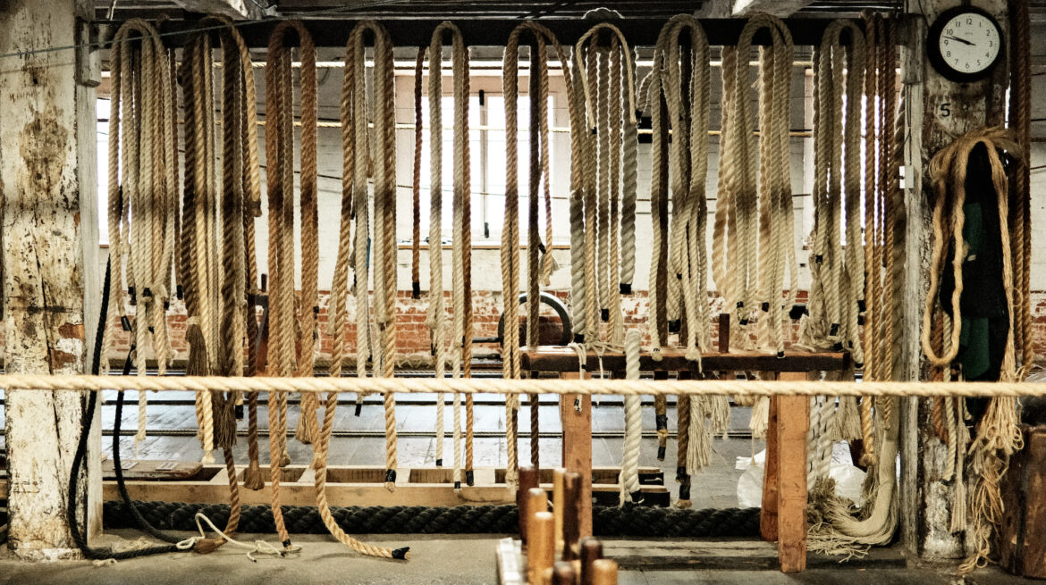 A row of hanging ropes in an industrial setting, with a clock and various tools in the background.